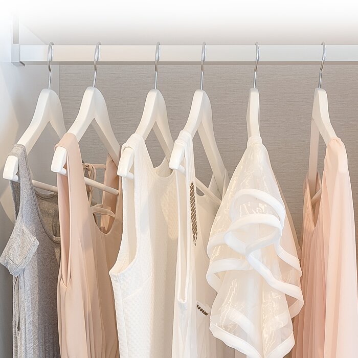Witte kleerhangers met neutrale kleding (wit, beige en grijs) aan een kledingroede in een kast, frontaal aanzicht