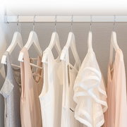 Witte kleerhangers met neutrale kleding (wit, beige en grijs) aan een kledingroede in een kast, frontaal aanzicht