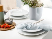 Elegantes Tafelservice mit weißen Tellern, blauer Serviette und Besteck, dekoriert mit Blumen und Kirschtomaten, seitliche Perspektive.