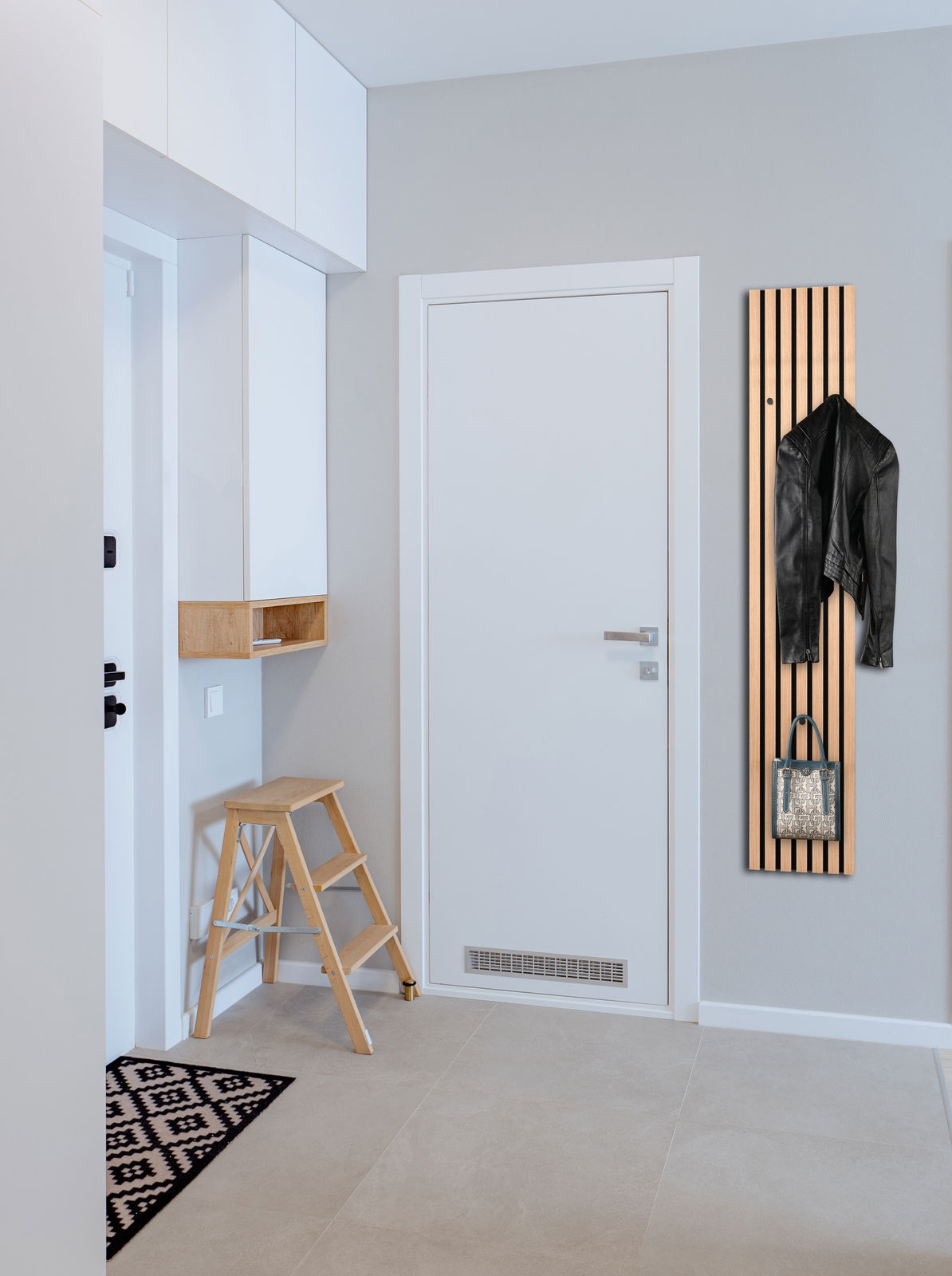 Schmale Wandgarderobe aus Holz mit vertikalen Streifen, an der eine schwarze Jacke und eine Tasche hängen. Perspektive von vorne.