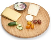 Rundes Drehkabinett aus Holz mit verschiedenen Käsesorten, Gurkenscheiben, Tomaten und einem Dip, von oben betrachtet.