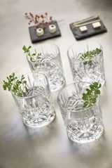 Vier Whiskygläser aus Kristallglas mit dekorativem Schliff, von oben fotografiert, mit grünen Zweigen als Dekoration.
