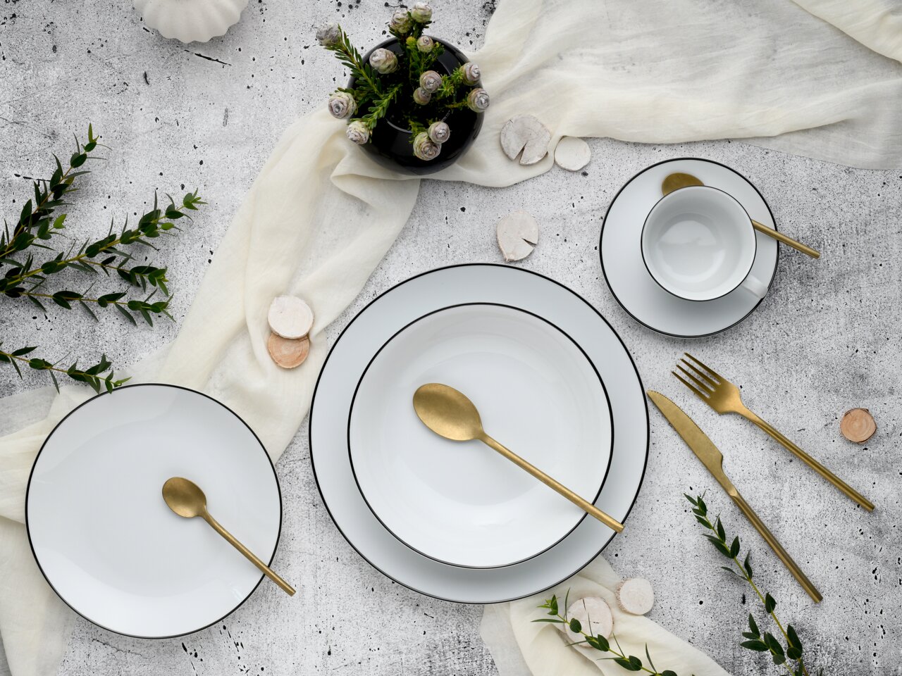 Elegantes Kombiservice 30-tlg. Luna Black L in Draufsicht, bestehend aus weißem Porzellan mit schwarzem Rand, dekoriert mit goldfarbenem Besteck und grünen Akzenten.