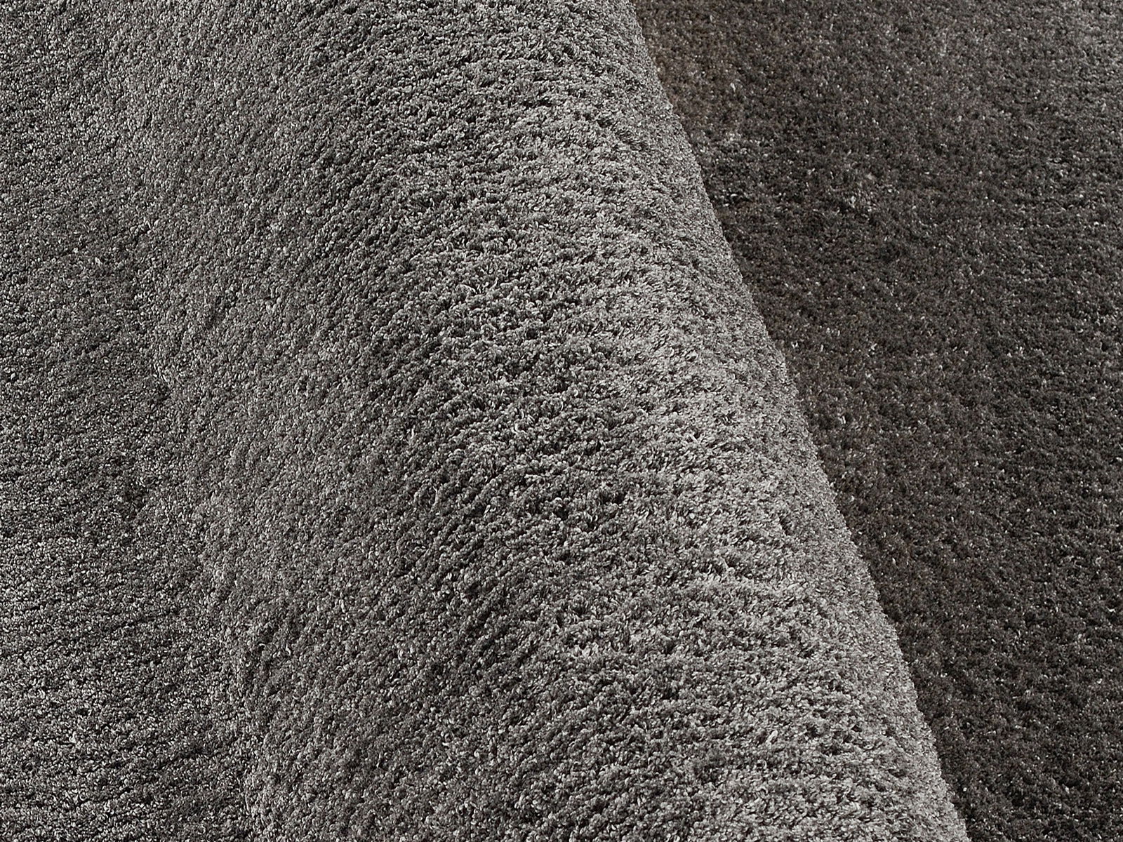 Nahaufnahme eines grauen Hochflor-Teppichs mit weicher, flauschiger Textur, seitliche Perspektive
