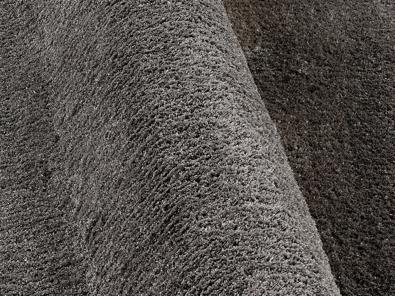 Nahaufnahme eines grauen Hochflor-Teppichs mit weicher, flauschiger Textur, seitliche Perspektive