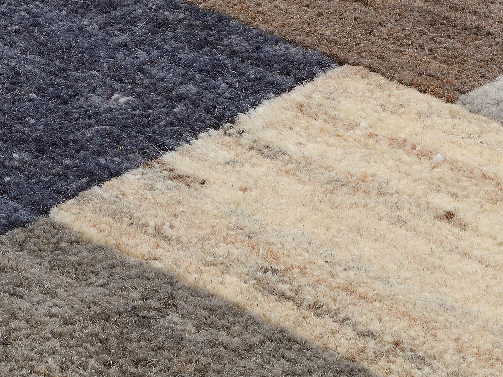Nahaufnahme eines Wollteppichs mit verschiedenen Farbfeldern in Blau, Braun und Beige aus der Vogelperspektive.
