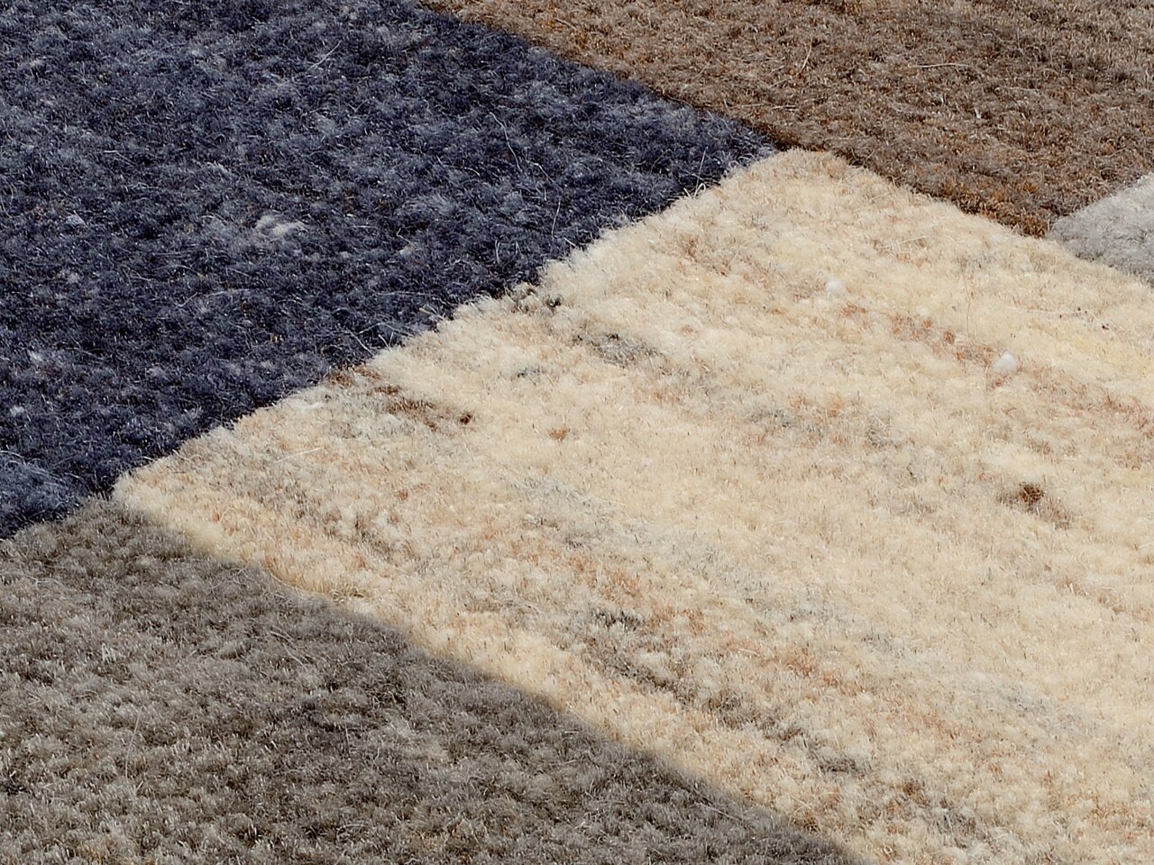 Nahaufnahme eines Wollteppichs mit verschiedenen Farbfeldern in Blau, Braun und Beige aus der Vogelperspektive.