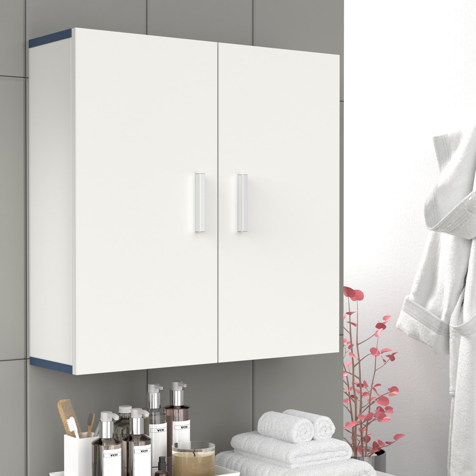 Weißer Badezimmer-Wandschrank mit zwei Türen und silbernen Griffen, leicht schräg von vorne (Frontansicht) an einer grauen Fliesenwand über einem Waschbeckenbereich.