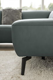 Nahaufnahme einer modernen Eckgarnitur in grauem Stoff mit schwarzen Metallfüßen, auf einem hellen Teppich stehend. Perspektive von der Seite.