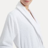 Nahaufnahme eines weißen Bademantels mit Schalkragen, getragen von einer Person, die von der Seite zu sehen ist.