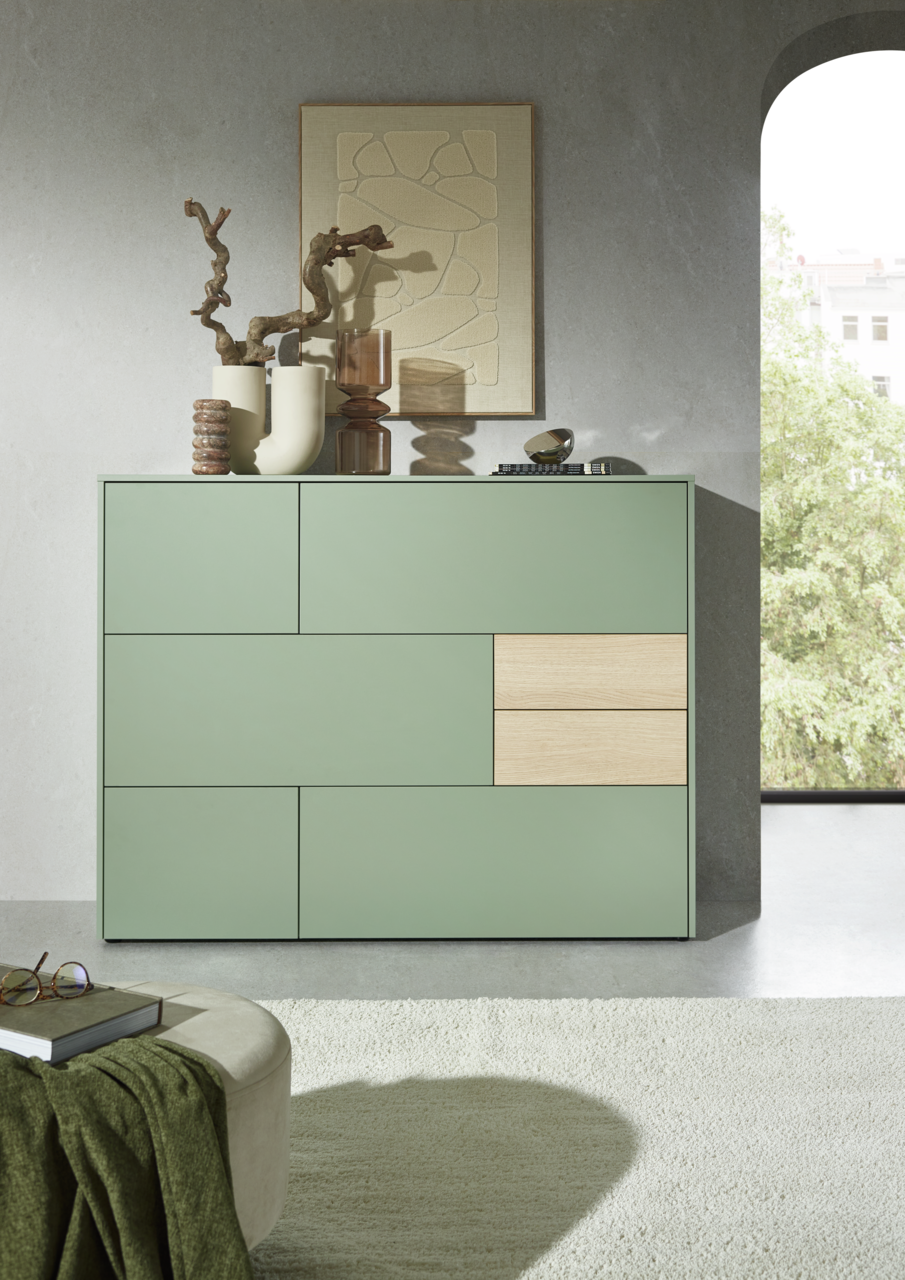Modernes Highboard in Salbeigrün mit Holzakzenten, dekoriert mit Vasen und Kunstobjekten, seitliche Perspektive
