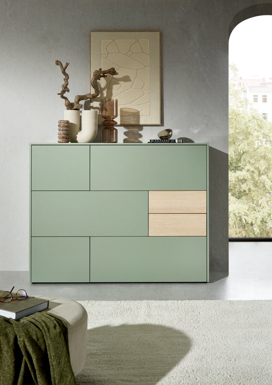 Modernes Highboard in Salbeigrün mit Holzakzenten, dekoriert mit Vasen und Kunstobjekten, seitliche Perspektive