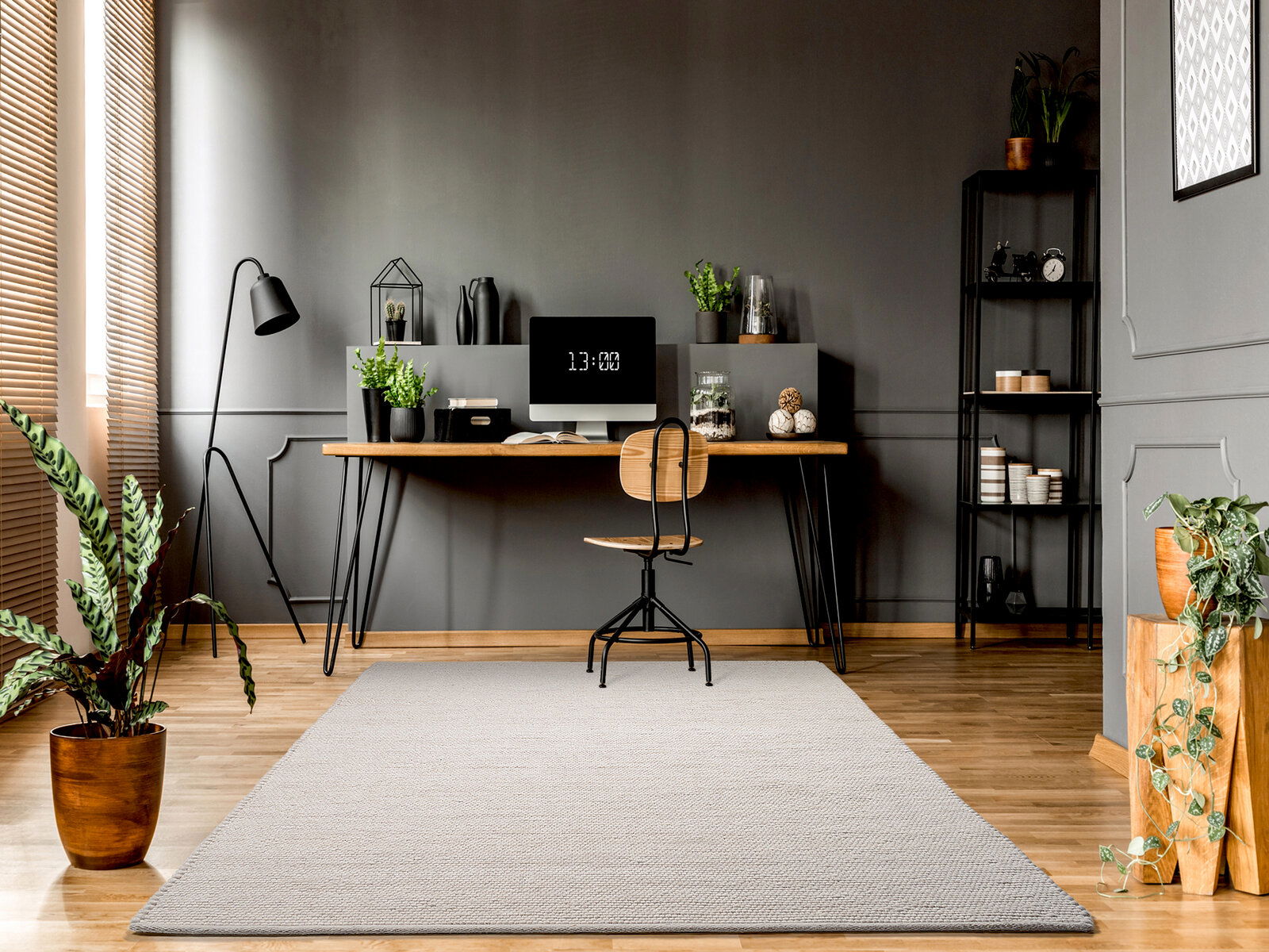 Moderner Arbeitsbereich mit einem hellgrauen Handwebteppich im Vordergrund, der auf einem Holzboden liegt. Der Raum ist stilvoll eingerichtet mit einem Schreibtisch, Pflanzen und Regalen. Perspektive von vorne auf den Teppich.