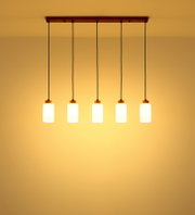 Moderne 5-flammige Pendelleuchte mit Holz-Deckenbalken, schwarzen Kabeln und zylindrischen weißen Glasschirmen, warm leuchtend, Frontalansicht von unten