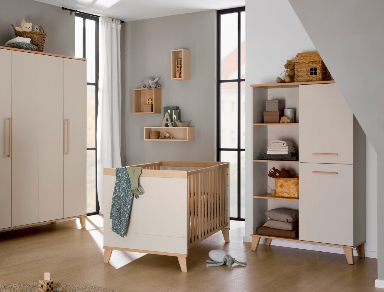 Modernes Kinderzimmer mit Standregal, Wickelkommode und Gitterbett aus hellem Holz, seitliche Perspektive