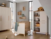 Modernes Kinderzimmer mit Standregal, Wickelkommode und Gitterbett aus hellem Holz, seitliche Perspektive