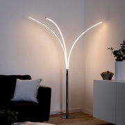Moderne Stehleuchte aus Chrom mit geschwungenen LED-Lichtarmen, in einer gemütlichen Wohnzimmerumgebung, seitliche Perspektive