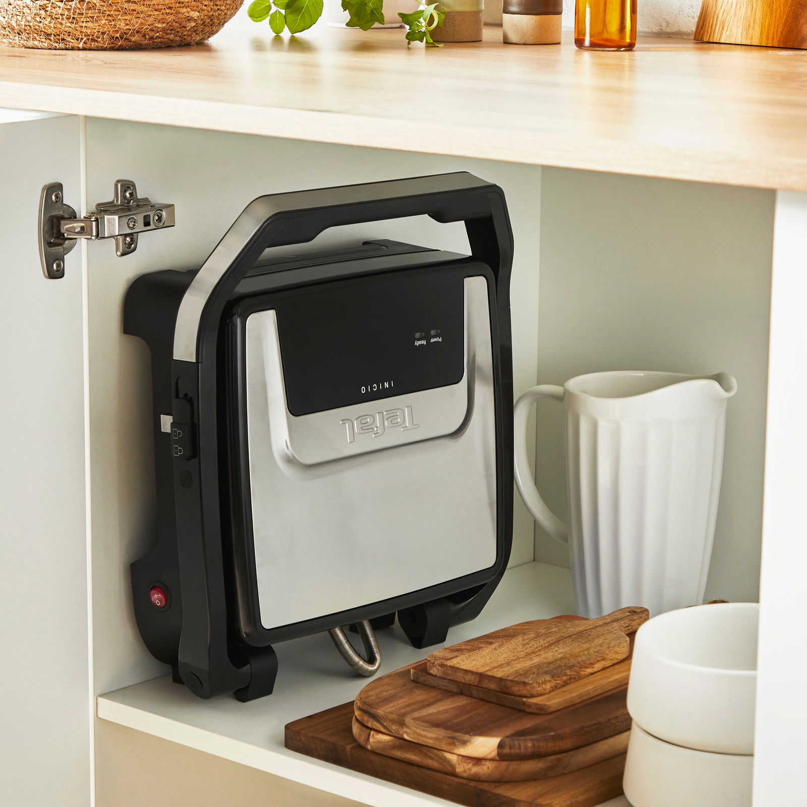 Kontaktgrill Classic GC271D in einem Küchenschrank, vertikal gelagert neben Küchenutensilien, aus seitlicher Perspektive.