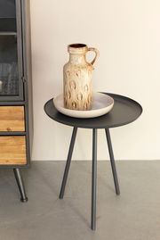 Moderner Beistelltisch mit schwarzer runder Tischplatte und drei Beinen, seitliche Perspektive, dekoriert mit einer Keramikvase und einer Schale.