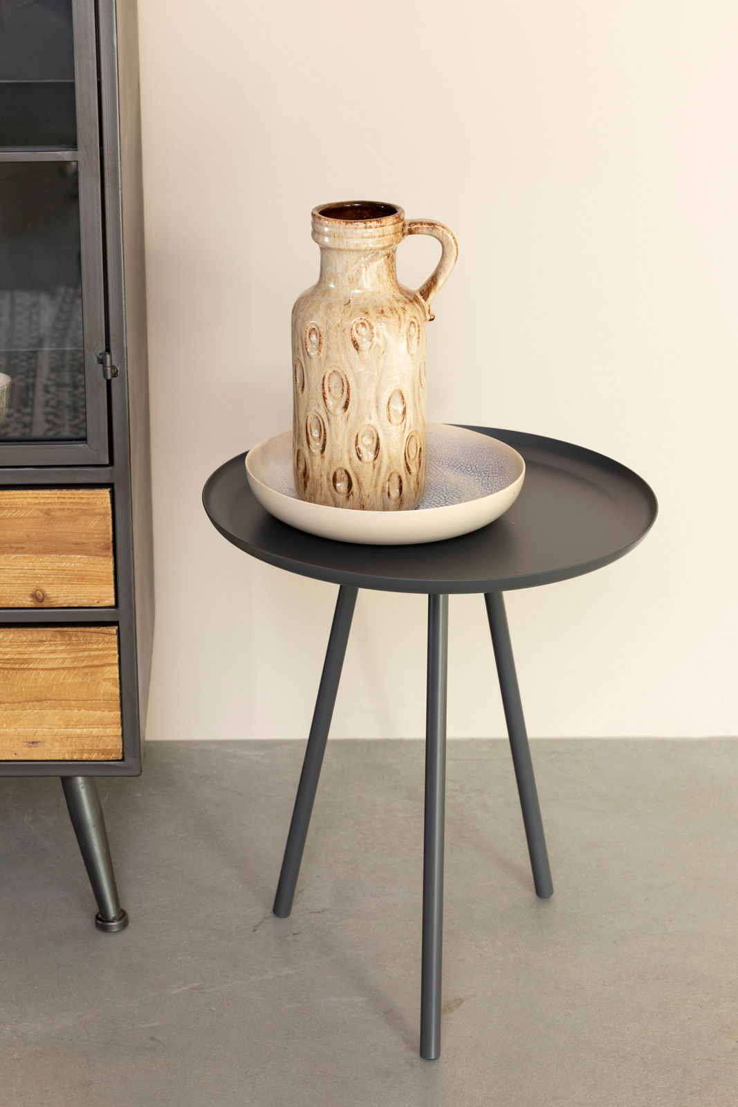 Moderner Beistelltisch mit schwarzer runder Tischplatte und drei Beinen, seitliche Perspektive, dekoriert mit einer Keramikvase und einer Schale.
