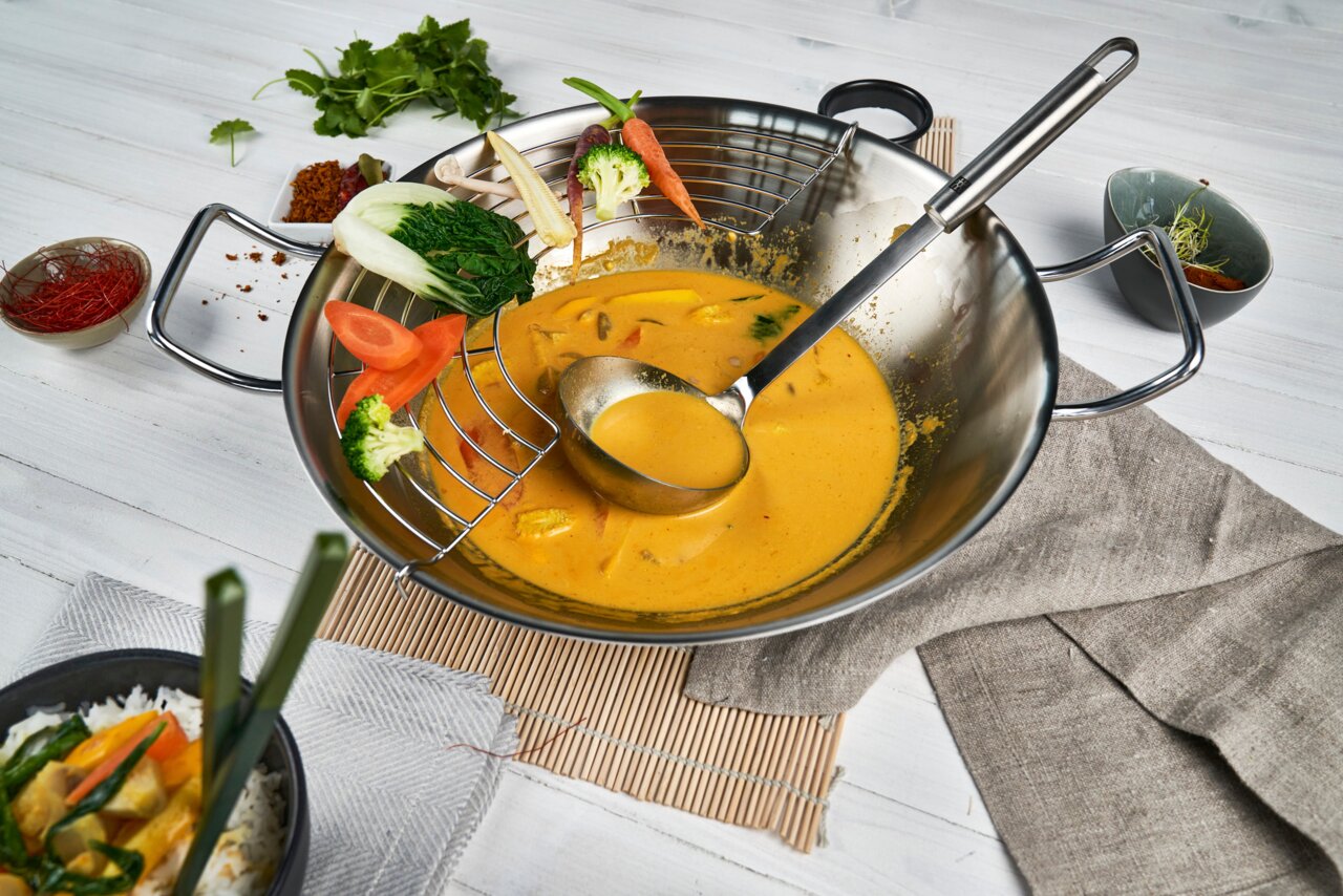 Schöpflöffel Pro in een wok met gele currysaus en verse groenten, van bovenaf gefotografeerd.