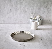 Obstbodenform aus Metall mit gewelltem Rand, auf einer Küchenarbeitsplatte aus Beton, im Vordergrund in der Draufsicht.