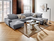 Graues Ecksofa in U-Form in einem modernen Wohnzimmer mit Holzboden, Glas-Couchtisch und großen Fenstern, seitliche Perspektive.