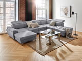 Graues Ecksofa in U-Form in einem modernen Wohnzimmer mit Holzboden, Glas-Couchtisch und großen Fenstern, seitliche Perspektive.