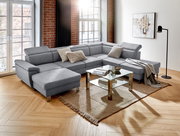 Graues Ecksofa in U-Form in einem modernen Wohnzimmer mit Holzboden, Glas-Couchtisch und großen Fenstern, seitliche Perspektive.