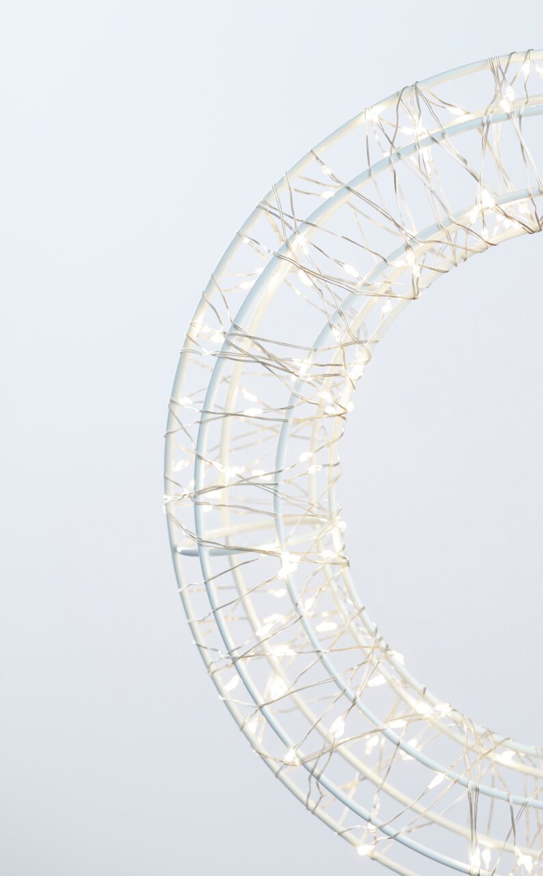 Nahaufnahme eines LED-Kranzes mit einem Durchmesser von 30 cm, umwickelt mit leuchtenden Lichterketten, seitliche Perspektive.