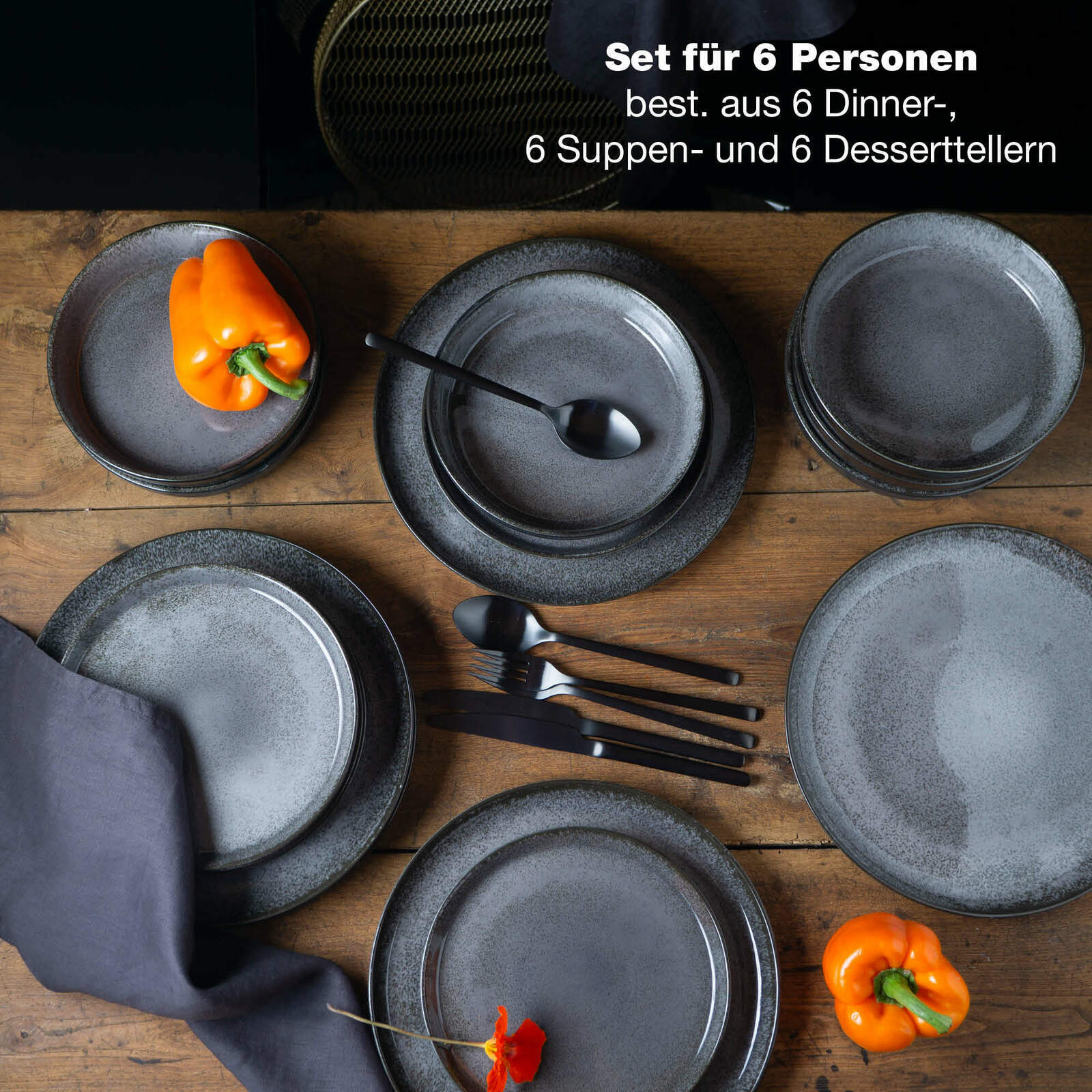 Vogelperspektive auf ein 18-teiliges Tafelservice in Anthrazit, bestehend aus 6 Dinner-, 6 Suppen- und 6 Desserttellern, dekoriert mit orangefarbenen Paprikas und Besteck.