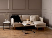 Moderner Couchtisch mit hellem Holz und schwarzem Metallgestell, frontal vor einem beigen Sofa in einem stilvoll eingerichteten Wohnzimmer.