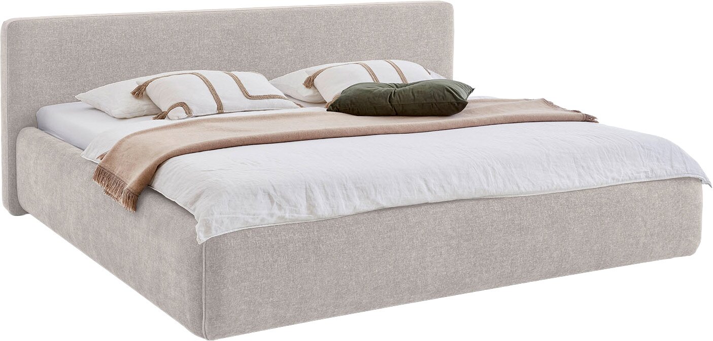 Modernes Polsterbett in hellem Beige mit hohem, weich gepolstertem Kopfteil und breitem Bettrahmen, dekoriert mit weißer Bettwäsche und Kissen, aus schräger Frontansicht