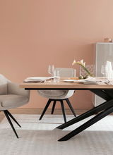 Moderner Esstisch mit Holzplatte und schwarzen Metallbeinen, umgeben von beigen Stühlen, gedeckt mit elegantem Geschirr und Gläsern, seitliche Perspektive.