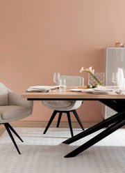 Moderner Esstisch mit Holzplatte und schwarzen Metallbeinen, umgeben von beigen Stühlen, gedeckt mit elegantem Geschirr und Gläsern, seitliche Perspektive.