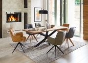 Moderner Esstisch mit Holzplatte und schwarzen Metallbeinen, umgeben von verschiedenen gepolsterten Stühlen in einem stilvollen Esszimmer mit Kamin. Perspektive: seitliche Ansicht.