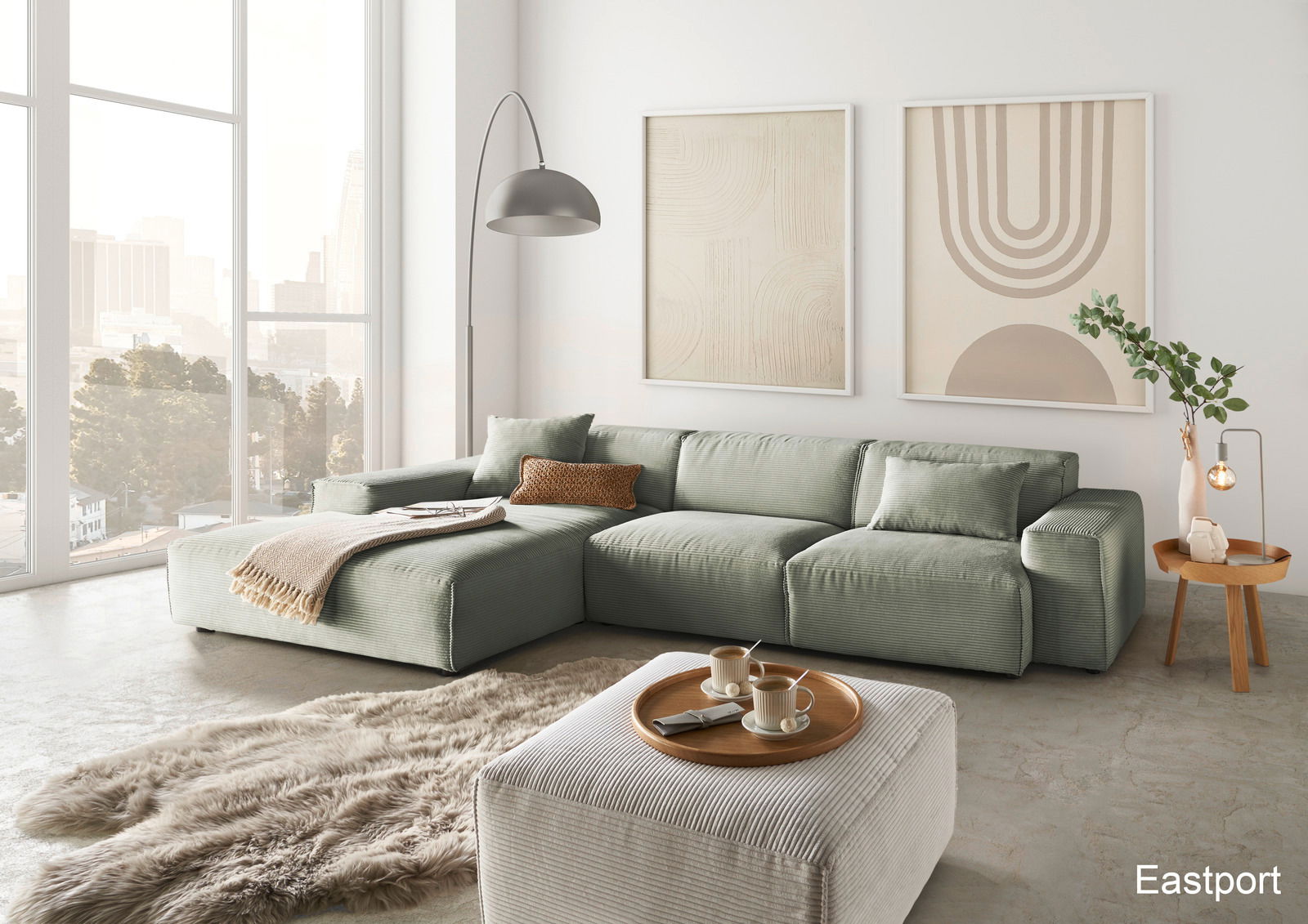 Moderne grüne Ecksofa-Landschaft in einem hellen Wohnzimmer mit großen Fenstern, einem flauschigen Teppich und einem Beistelltisch. Perspektive von vorne links.