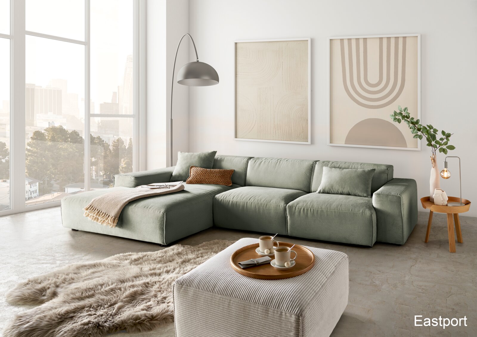 Moderne grüne Ecksofa-Landschaft in einem hellen Wohnzimmer mit großen Fenstern, einem flauschigen Teppich und einem Beistelltisch. Perspektive von vorne links.