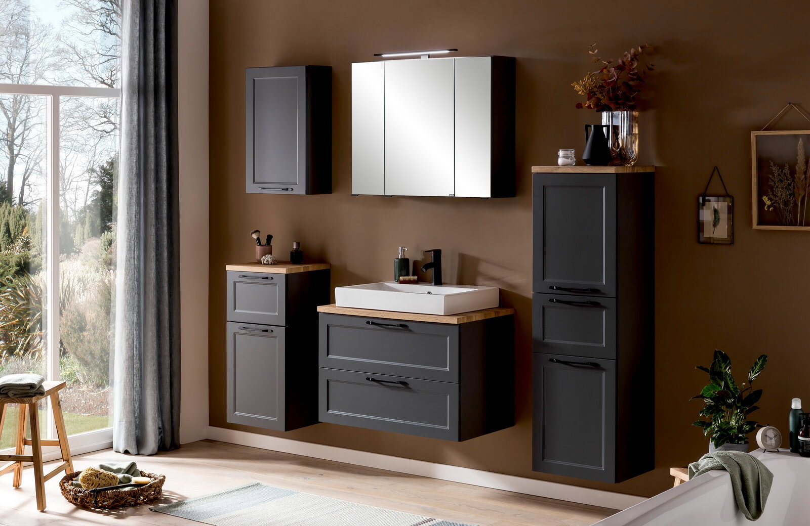 Moderne Badezimmermöbel in dunklem Grau mit Holzoberflächen, bestehend aus einem Midischrank, einem Waschbeckenunterschrank und einem Spiegelschrank, seitliche Perspektive.