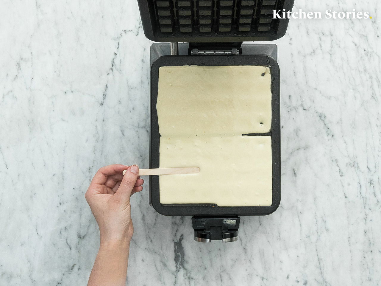 Waffeleisen Professional von oben mit Teig gefüllt, eine Hand hält einen Holzstab.