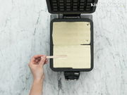 Waffeleisen Professional von oben mit Teig gefüllt, eine Hand hält einen Holzstab.