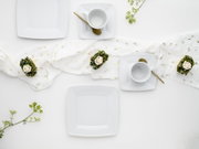 Elegantes weißes, quadratisches Geschirr-Set mit Tellern und Tassen auf hellem Tisch, goldene Löffel und florale Deko; Draufsicht von oben (Flatlay).
