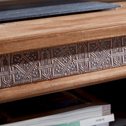 Nahaufnahme eines TV-Tisches mit dekorativem, geschnitztem Holzdetail und einer Zeitschrift im Regal darunter, seitliche Perspektive.
