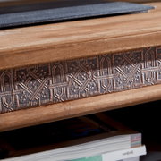 Close-up van een tv-meubel met een decoratief, bewerkt houten detail en een tijdschrift op de plank eronder, gezien vanuit de zijkant.