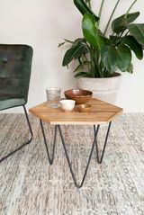 Beistelltisch mit Holzplatte und Metallbeinen, dekoriert mit Schalen und Glas, neben einem grünen Sessel und einer großen Zimmerpflanze, aus der Perspektive von vorne.