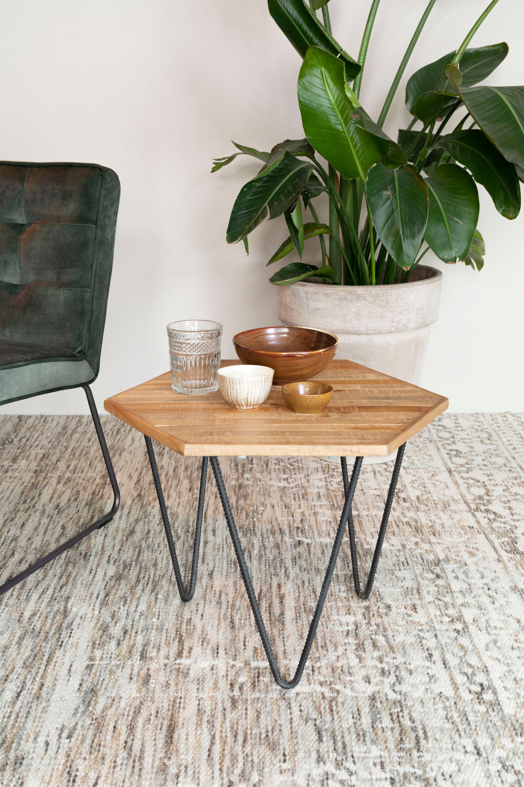 Z2 Beistelltisch COR Beistelltisch mit Holzplatte und Metallbeinen, dekoriert mit Schalen und Glas, neben einem grünen Sessel und einer großen Zimmerpflanze, aus der Perspektive von vorne.
