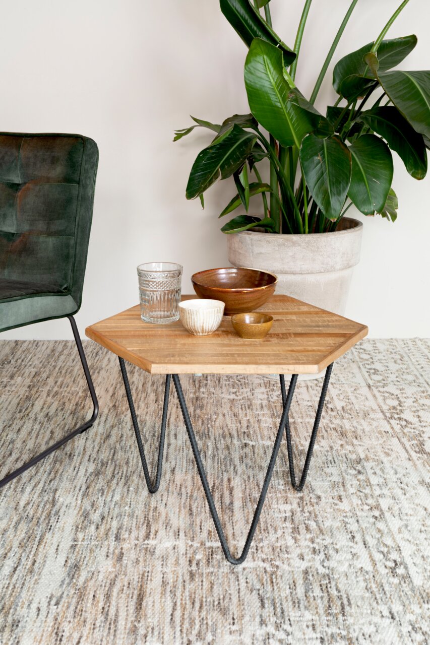 Beistelltisch mit Holzplatte und Metallbeinen, dekoriert mit Schalen und Glas, neben einem grünen Sessel und einer großen Zimmerpflanze, aus der Perspektive von vorne.
