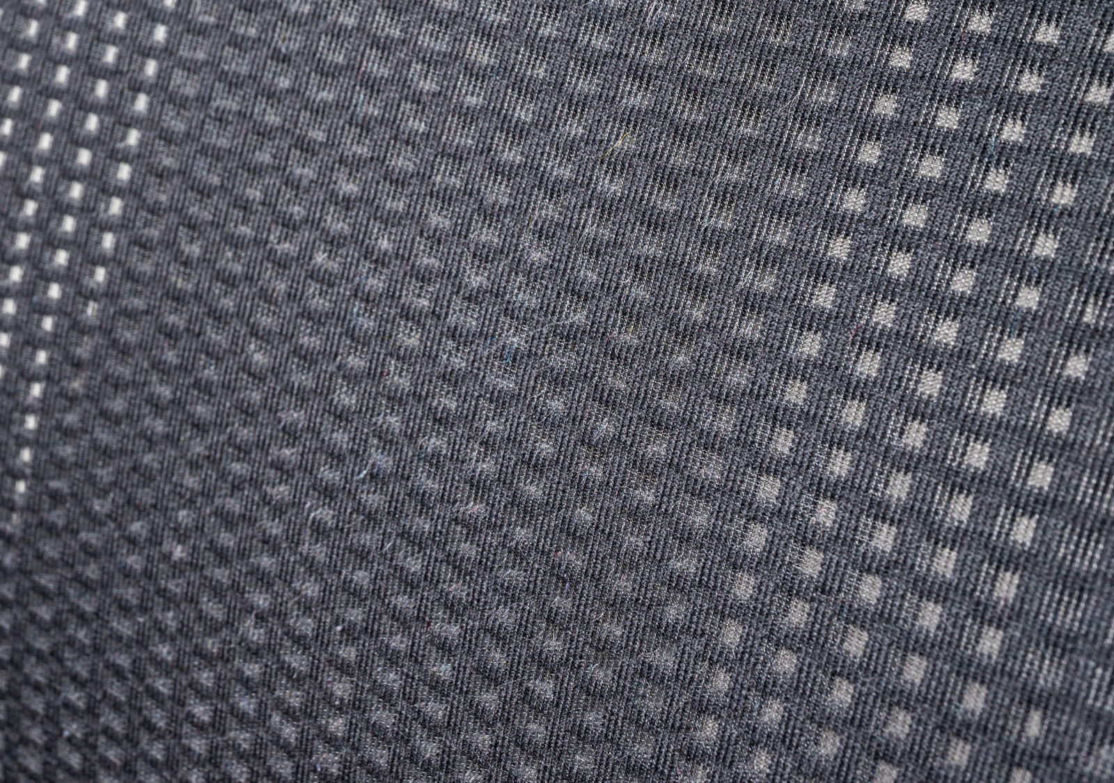 Nahaufnahme eines grauen Stoffmusters mit kleinen quadratischen Mustern, perspektivisch von der Seite aufgenommen.