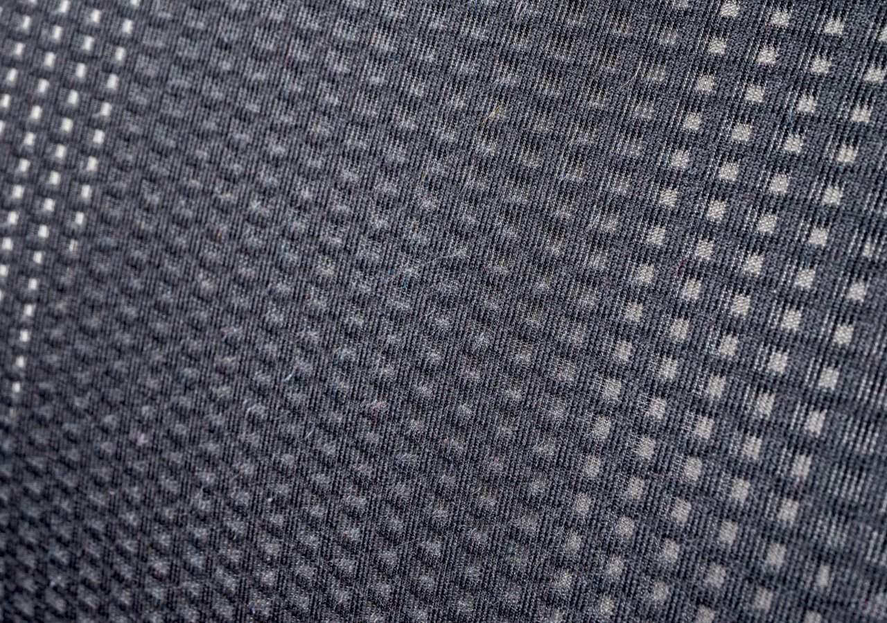 Nahaufnahme eines grauen Stoffmusters mit kleinen quadratischen Mustern, perspektivisch von der Seite aufgenommen.