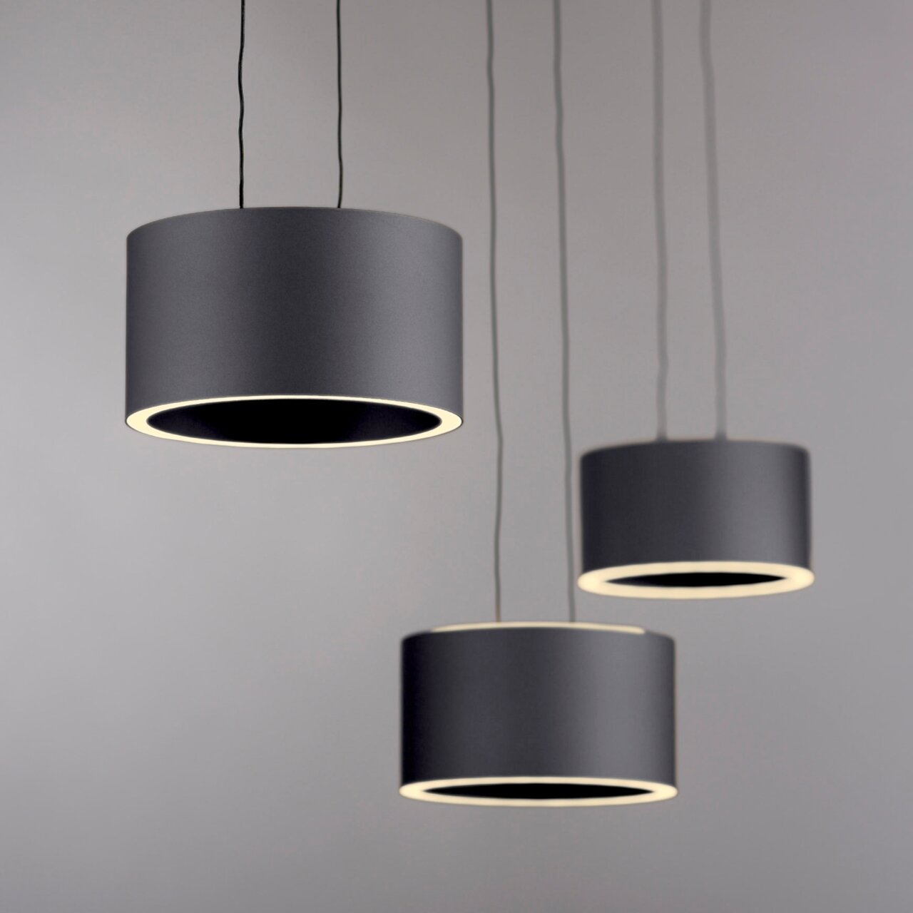 Drei moderne, zylindrische LED-Pendelleuchten in Schwarz, von unten betrachtet, mit warmem Lichtschein.